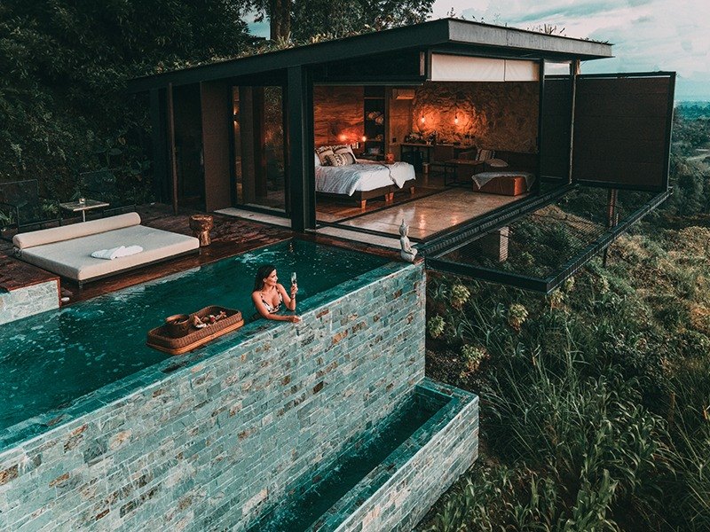 The terrace pool at dusk, its edge running out over the hillside, with the lit bedroom of the suite open behind it.